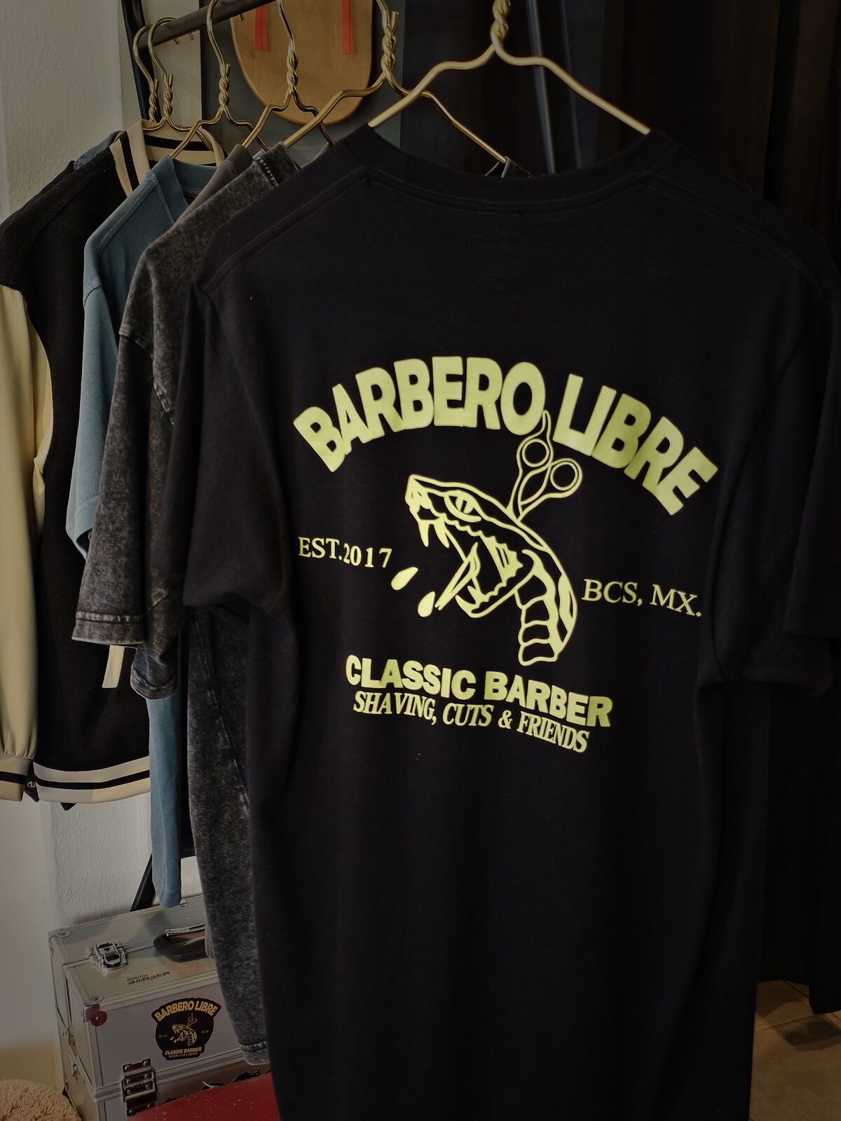 Playera negra de Barbero Libre con estampado verde lima: una serpiente con tijeras y el texto “Classic Barber · Shaving, cuts & friends · Est. 2017 · BCS, MX”.